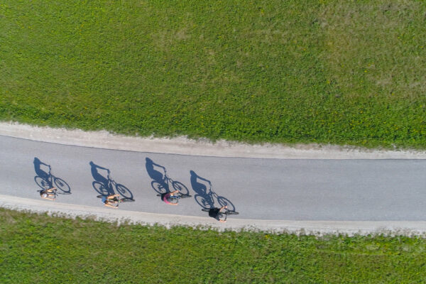 Top Down: Four Friends Riding Bikes Casting Shadows On The Empty Asphalt Road.